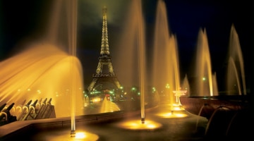 Fountains shimmering in the lights at night with the eiffel tower in the background