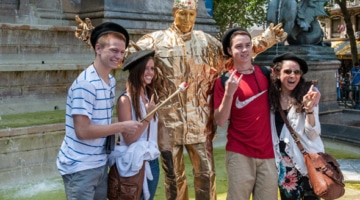 Young students taking a picture with a mime on a golden costume