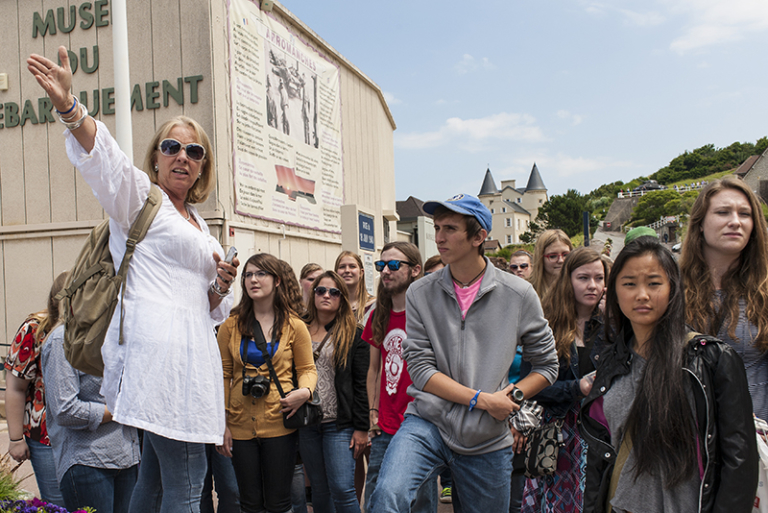 ACIS Tour Manager gesturing with a group next to the Musée du Débarquement in France