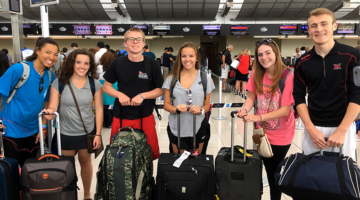Students pose for the camera in the airport with their suitcases
