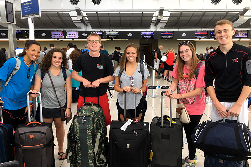 Students pose for the camera in the airport with their suitcases