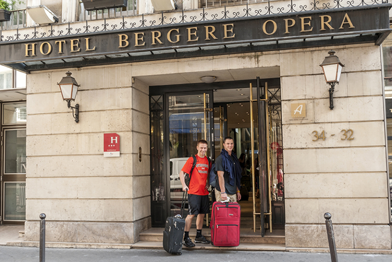 Two students holding suitcases enter the Hotel Bergere Opera